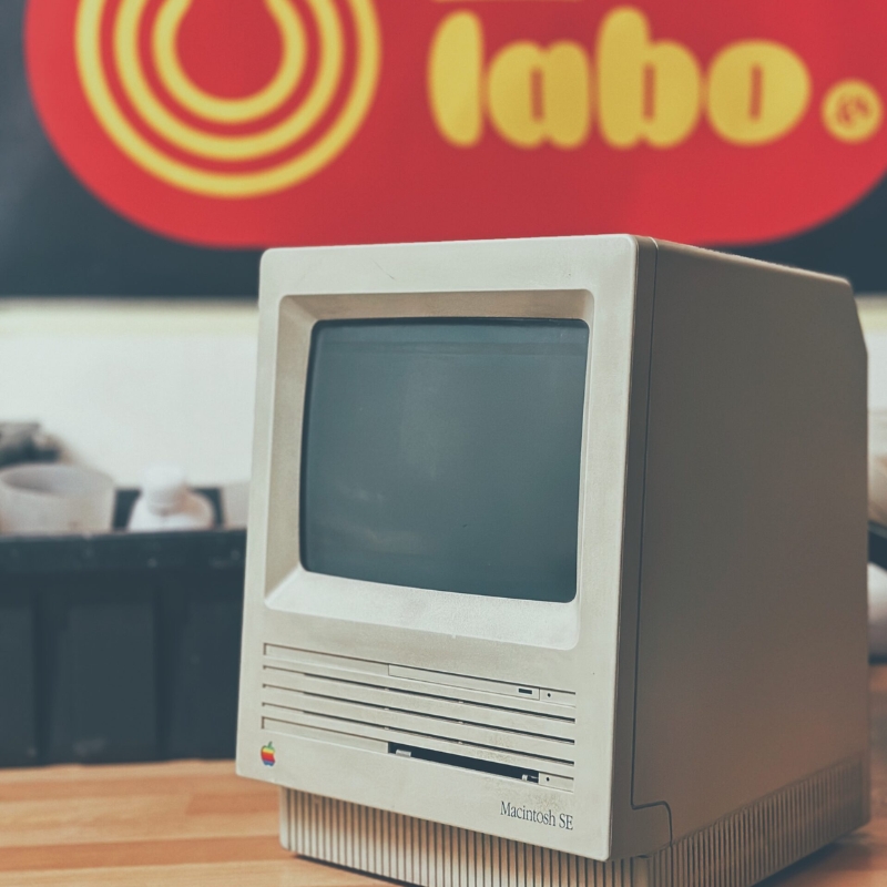 Ancien ordinateur Macintosh posé sur une paillasse sous l'enseigne rouge et jaune du labo