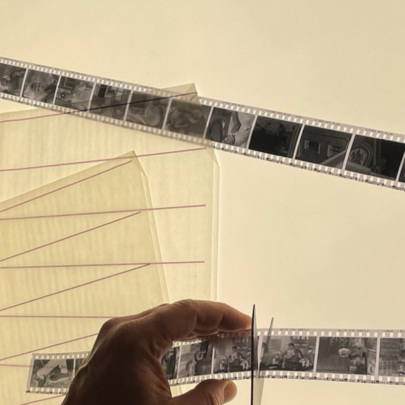 developpement-scan-negatifs-35mm-decoupe Négatifs noir et blanc 35 mm découpés en bandes sur une table lumineuse, à côté de pochettes en papier cristal