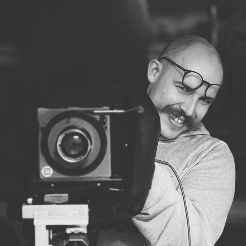 Matthieu, formateur du labo, souriant derrière une chambre photographique grand format