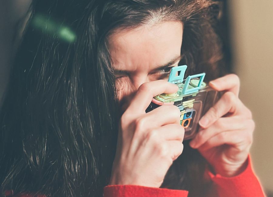 Une photographe en pull rouge vise à travers un petit appareil argentique transparent pendant un photowalk