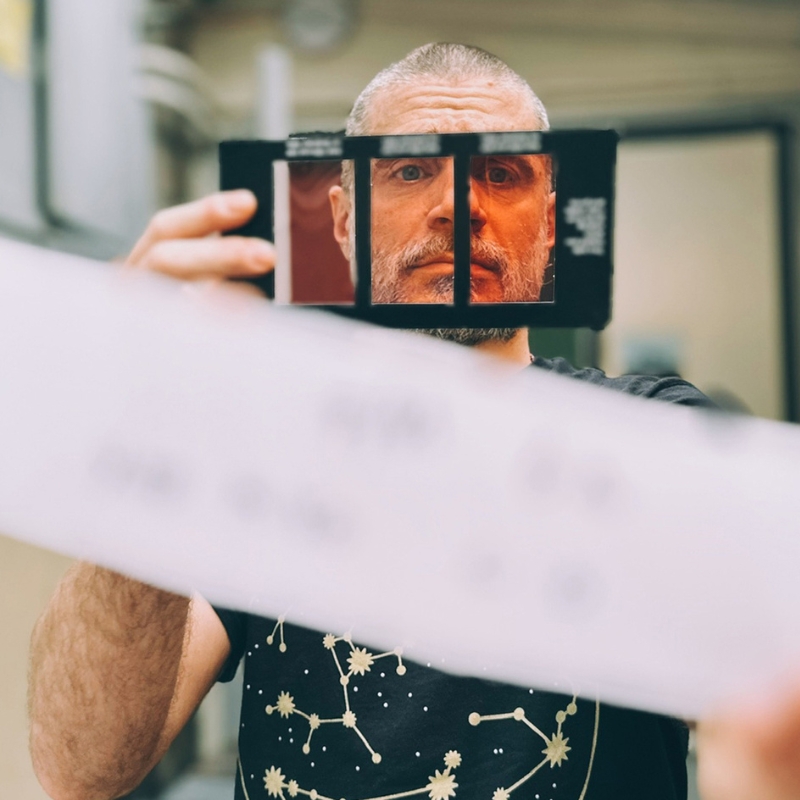 tirage-couleur-papier-rc-negatif Homme qui regarde à travers un négatif couleur tenu devant son visage